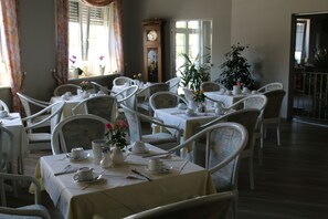Un comedor con varias mesas dispuestas para servicio de té, sillas blancas y un reloj grande en la pared.