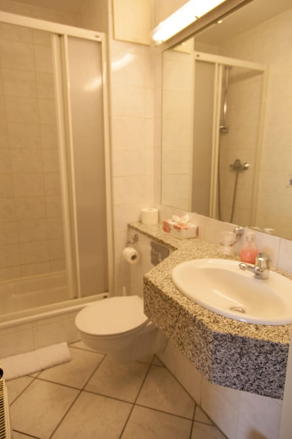 Un baño con ducha, inodoro, lavamanos y espejo.