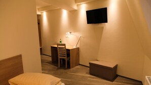A small, well-lit bedroom with a bed, a desk, and a TV mounted on the wall. - Hotel Moerser Hof (Moers)
