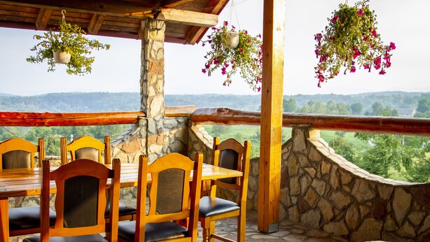 A wooden dining table with chairs, stone walls, and hanging flower baskets.