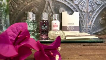 A wooden surface with three bottles of Molton Brown body wash, a pink orchid, and a white bar of soap.