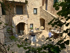 A stone courtyard with a table and chairs, surrounded by buildings with arched doorways and windows. - Villa Vager Mani (West Mani)