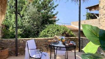 Un patio con una mesa preparada para el desayuno, rodeado de muros de piedra y follaje.