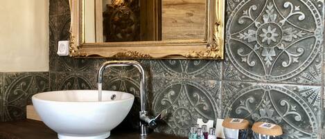 A bathroom with a large white vessel sink, a gold-framed mirror, and decorative tiles.