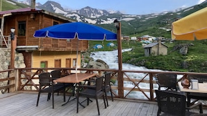 A wooden cabin with a deck, a blue umbrella, and a view of a mountain stream. - Yedigoller Hotel & Restaurant (Çaykara)