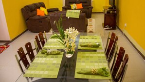 A dining area with a table set for four, surrounded by chairs, and a sofa in the background. - Milimani Furnished Elegant Apartments (Nakuru)