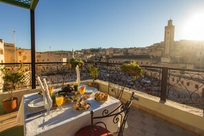 A rooftop dining area with a table set for two, overlooking a cityscape with a prominent tower.