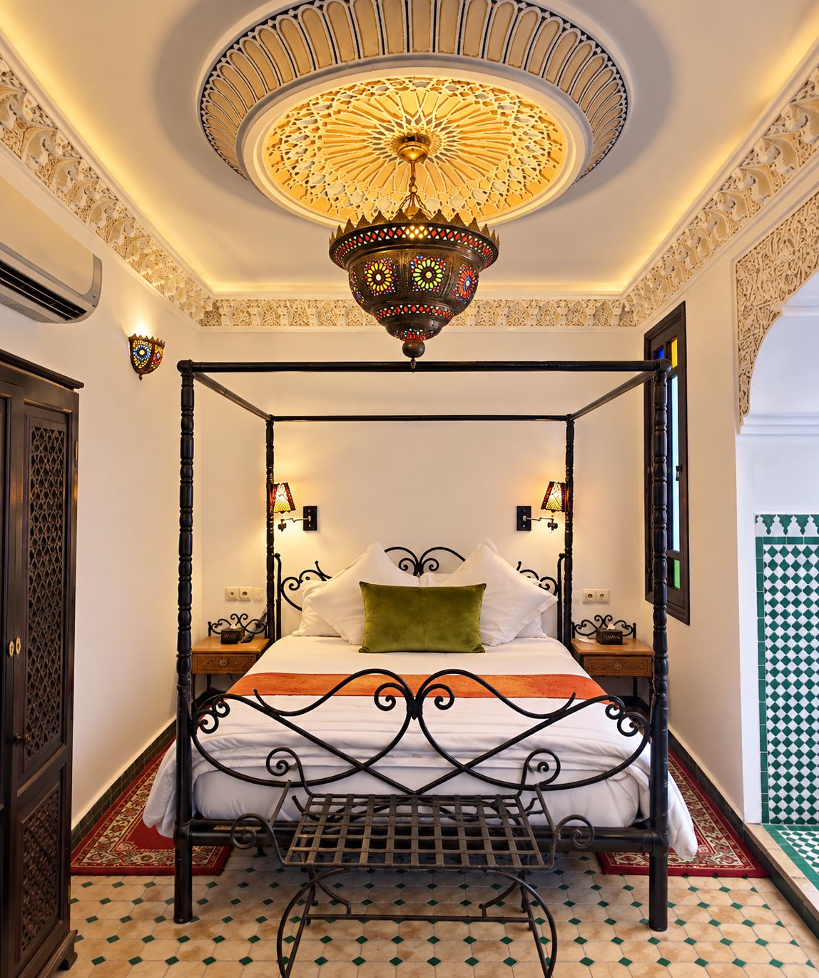 A four-poster bed with a decorative ceiling light, a patterned floor, and a wall-mounted lamp.
