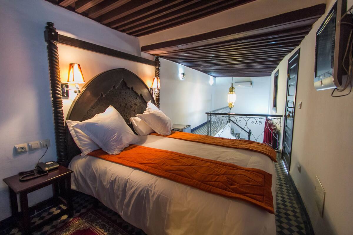 Uma cama de casal com um edredom laranja, uma cabeceira de madeira e uma mesa de cabeceira com abajur.