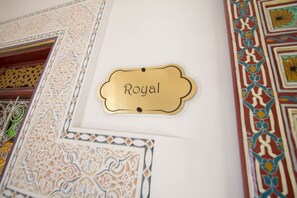 Uma placa dourada com a palavra 'Royal' numa parede branca, rodeada por desenhos complexos e ornamentados.