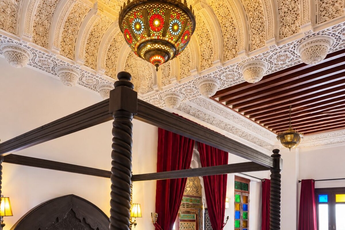 Uma cama de dossel com dossel, um candelabro e um quarto com padrões intrincados no teto.
