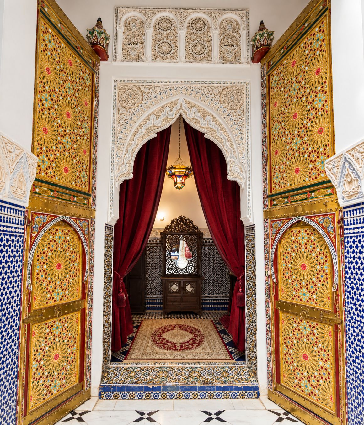 An ornate entryway with intricate tile work, red drapes, and a chandelier.