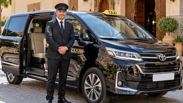 Una camioneta negra con un letrero que dice 'TAXI' estacionada frente a un edificio de arquitectura ornamentada.