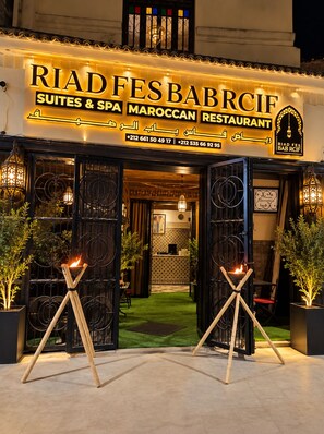 Das Äußere des Riad Fes Bab Rcif, ein marokkanisches Restaurant mit einem Schild, Telefonnummern und zwei offenen Eingängen.