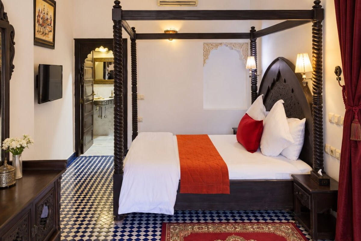 Una cama con dosel con un edredón rojo y blanco, un plaid rojo y una alfombra estampada.
