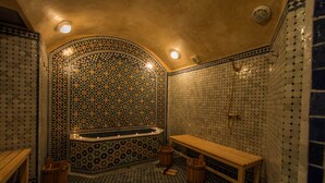 Un bany tradicional amb una banyera independent, seients de fusta i parets de rajola amb un disseny decoratiu.