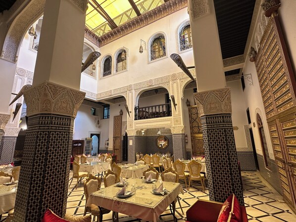 An interior with ornate arches, high ceilings, and a central open space with tables and chairs.