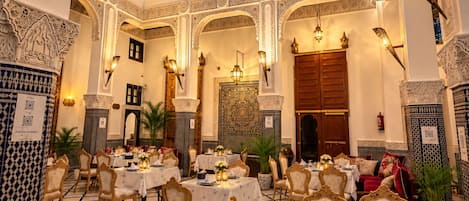 Un comedor amplio con varias mesas y sillas, detalles arquitectónicos ornamentales y un techo alto con tragaluces.