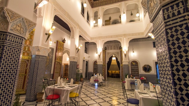 Un interior espaiós amb sostres alts, arcs ornamentals i un paviment de rajoles amb disseny. Taules preparades per dinar amb cadires, i la sala destaca per columnes decoratives i obra mural.