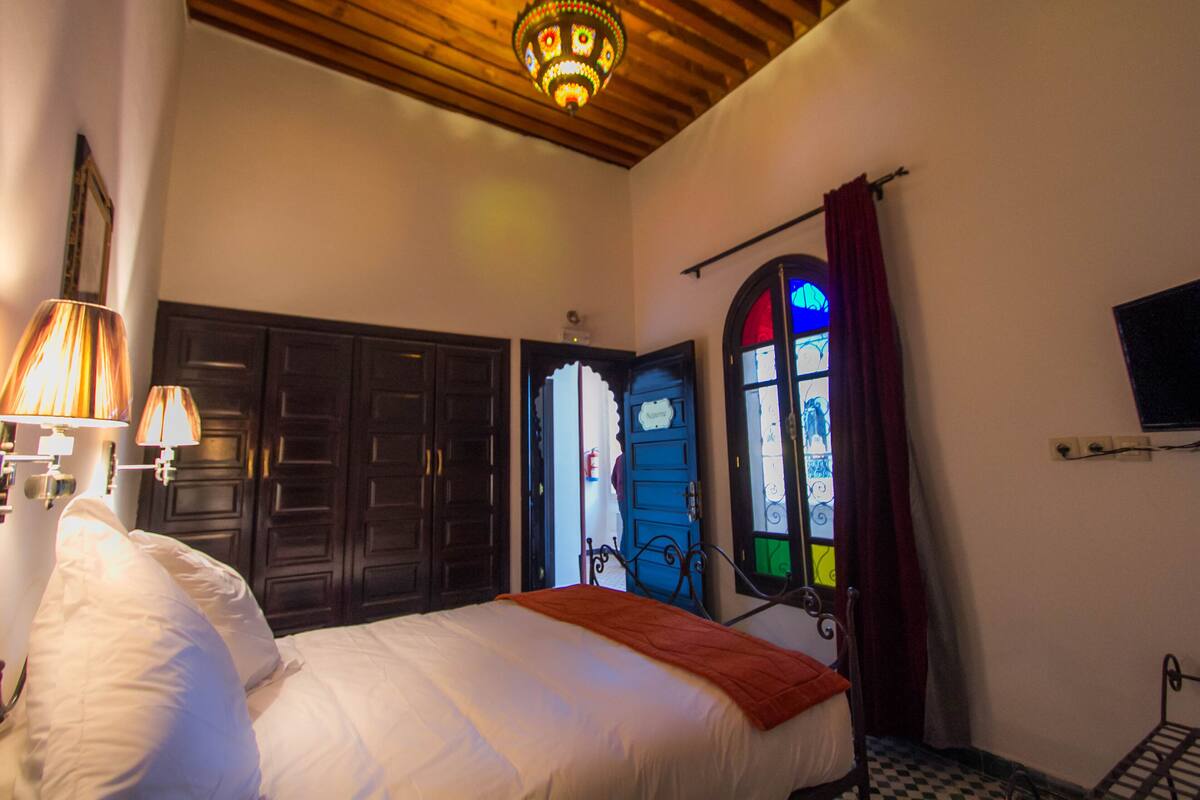 Quarto com cama, mesa de cabeceira, luminária, guarda-roupa e janela com vista.