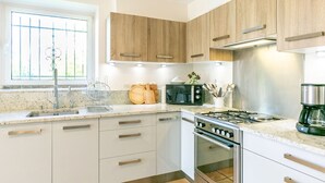 Une cuisine moderne avec des armoires blanches, un évier en acier inoxydable, un four à micro-ondes, une cuisinière à gaz et une machine à café.