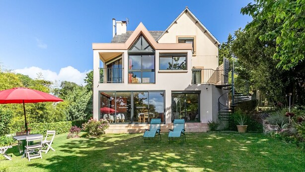 Une maison moderne à deux étages, dotée d’une grande baie vitrée, d’un balcon et d’une pelouse bien entretenue.