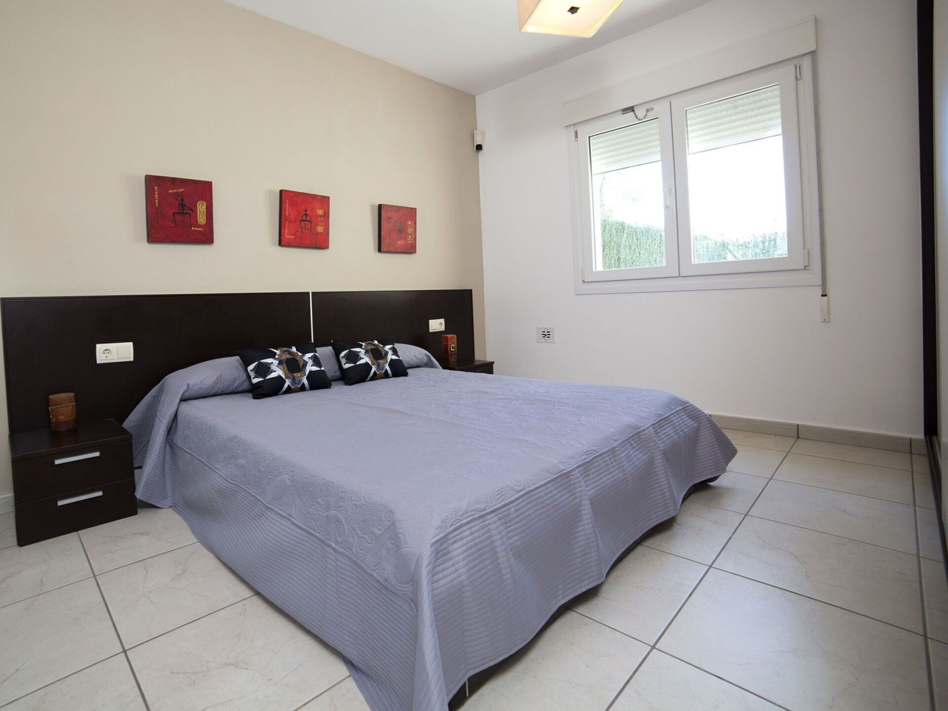 A bedroom with a bed, nightstands, a window, and three wall-mounted artworks.