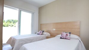 Hotellihuone, jossa on kaksi erillistä sänkyä, puinen pääty ja liukuovi, joka johtaa ulkotilalle.