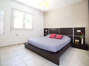 A modern bedroom with a bed, a nightstand, a window, and a wall-mounted light fixture. - Wonderful  villa for 6 guests with WIFI, A/C, pool, TV and patio (Benissa)