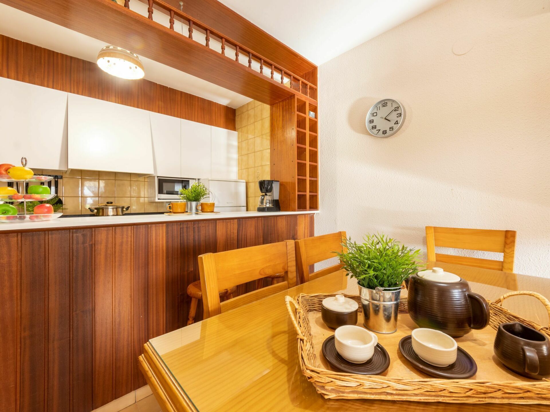 A modern kitchen with wooden cabinets, a built-in microwave, and a clock on the wall.