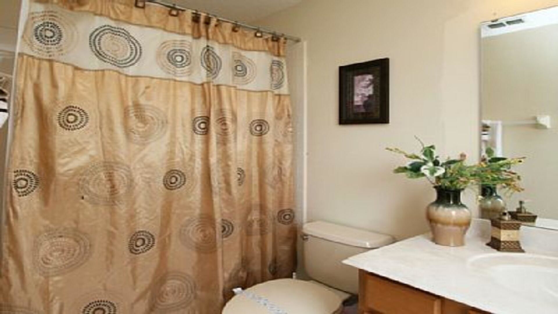 A bathroom with a beige patterned shower curtain, a white sink, and two vases with plants.