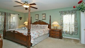 Une chambre à coucher avec un lit à baldaquin, une table de chevet, une lampe et un ventilateur de plafond.