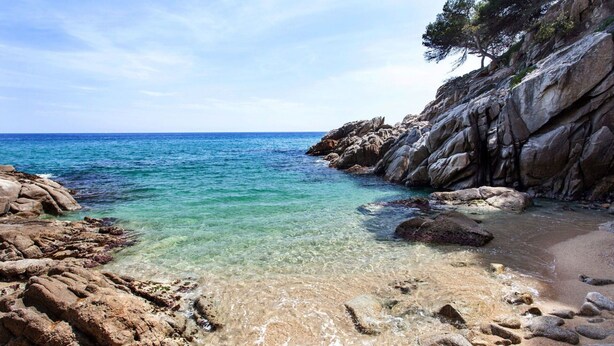 Une plage de galets bordée d’une eau turquoise et limpide, et d’une falaise rocheuse.