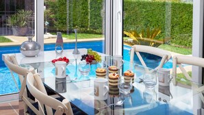 Une table en verre donnant sur une piscine, avec des sièges d’extérieur et un ciel dégagé.