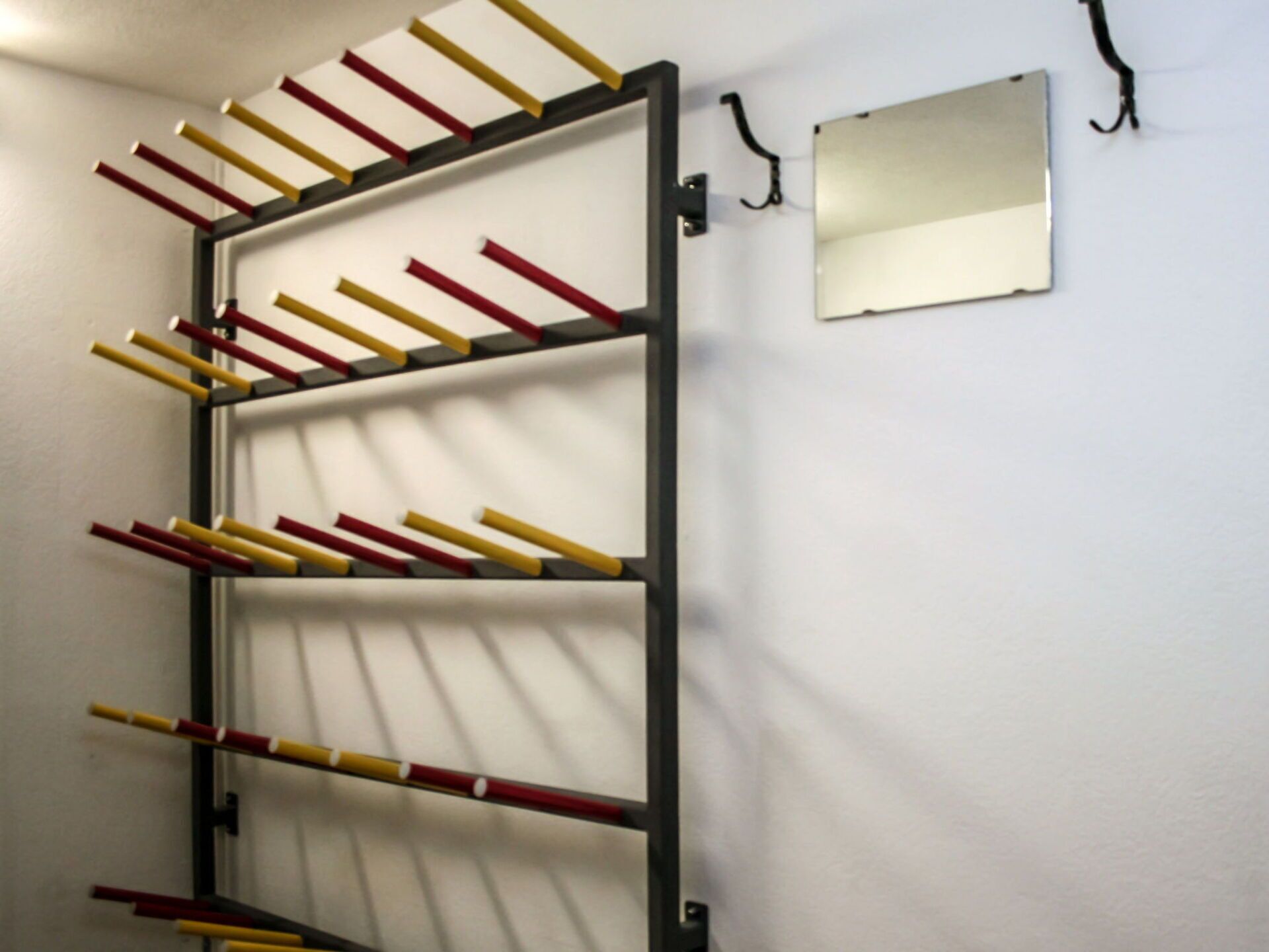 Uma estante fixada na parede com várias barras horizontais segurando objetos vermelhos e amarelos.