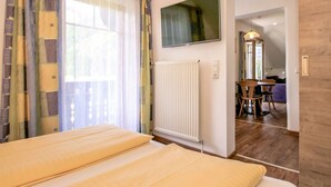 A hotel room with a bed, a TV mounted on the wall, a radiator, and a view of a dining area.