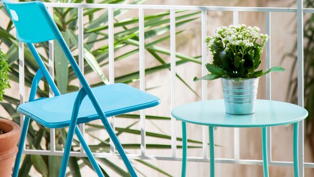 Un balcon avec une chaise bleue, une petite table et un pot de fleurs.