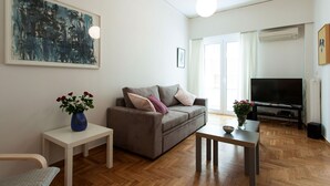 Un salon avec un canapé, une petite table, un téléviseur et un tableau accroché au mur.