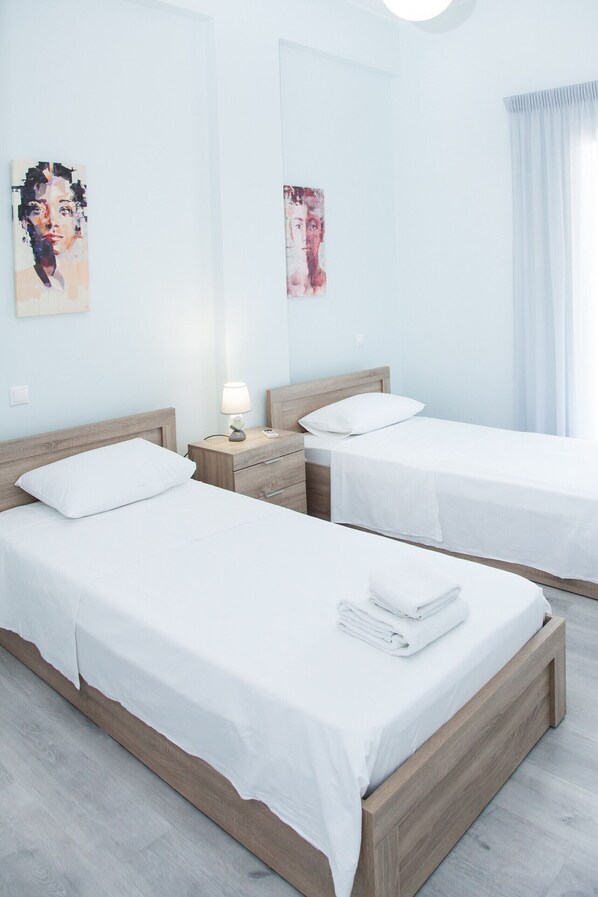 Une chambre d’hôtel avec deux lits simples, une tête de lit en bois, une table de chevet avec une lampe et des œuvres d’art accrochées aux murs.