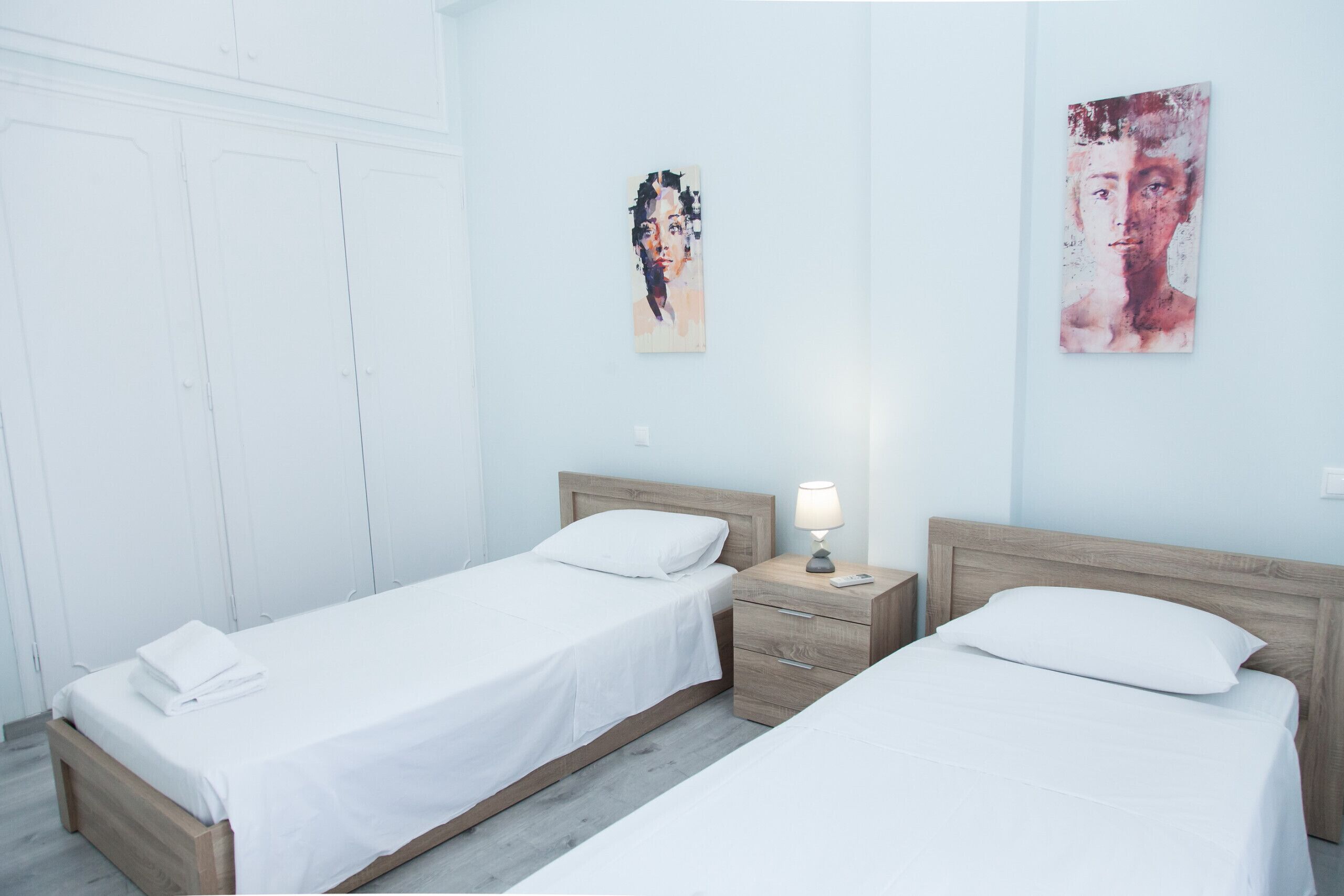 A hotel room with two single beds, a nightstand with a lamp, and a wall-mounted artwork.
