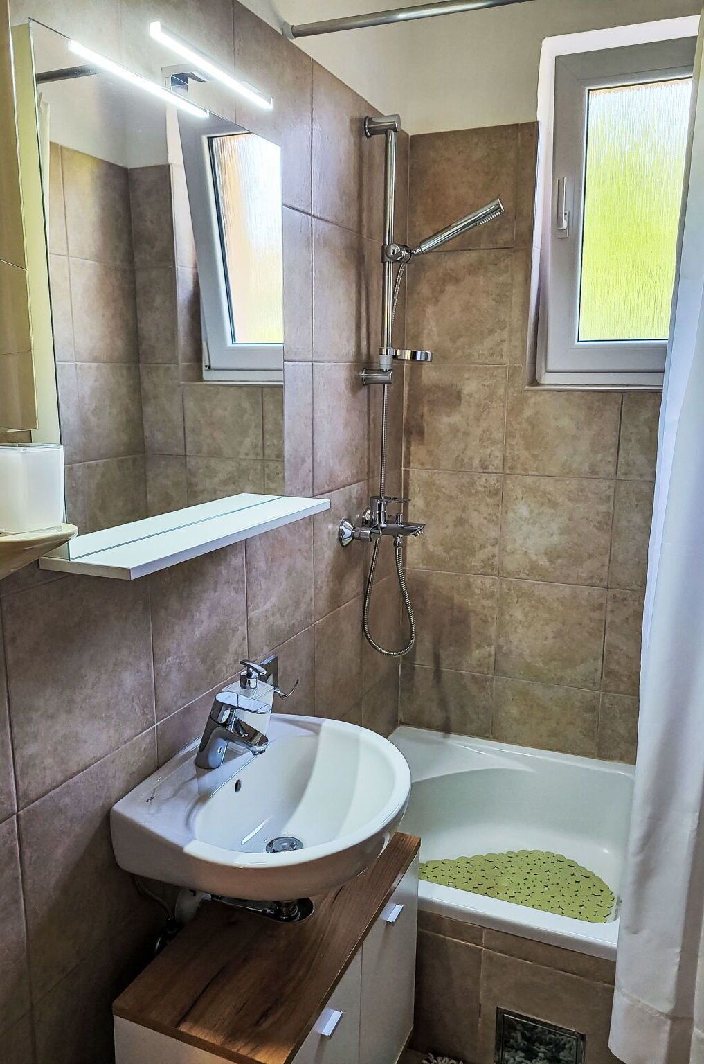 Een moderne badkamer met een wastafel, spiegel, douche en bad.