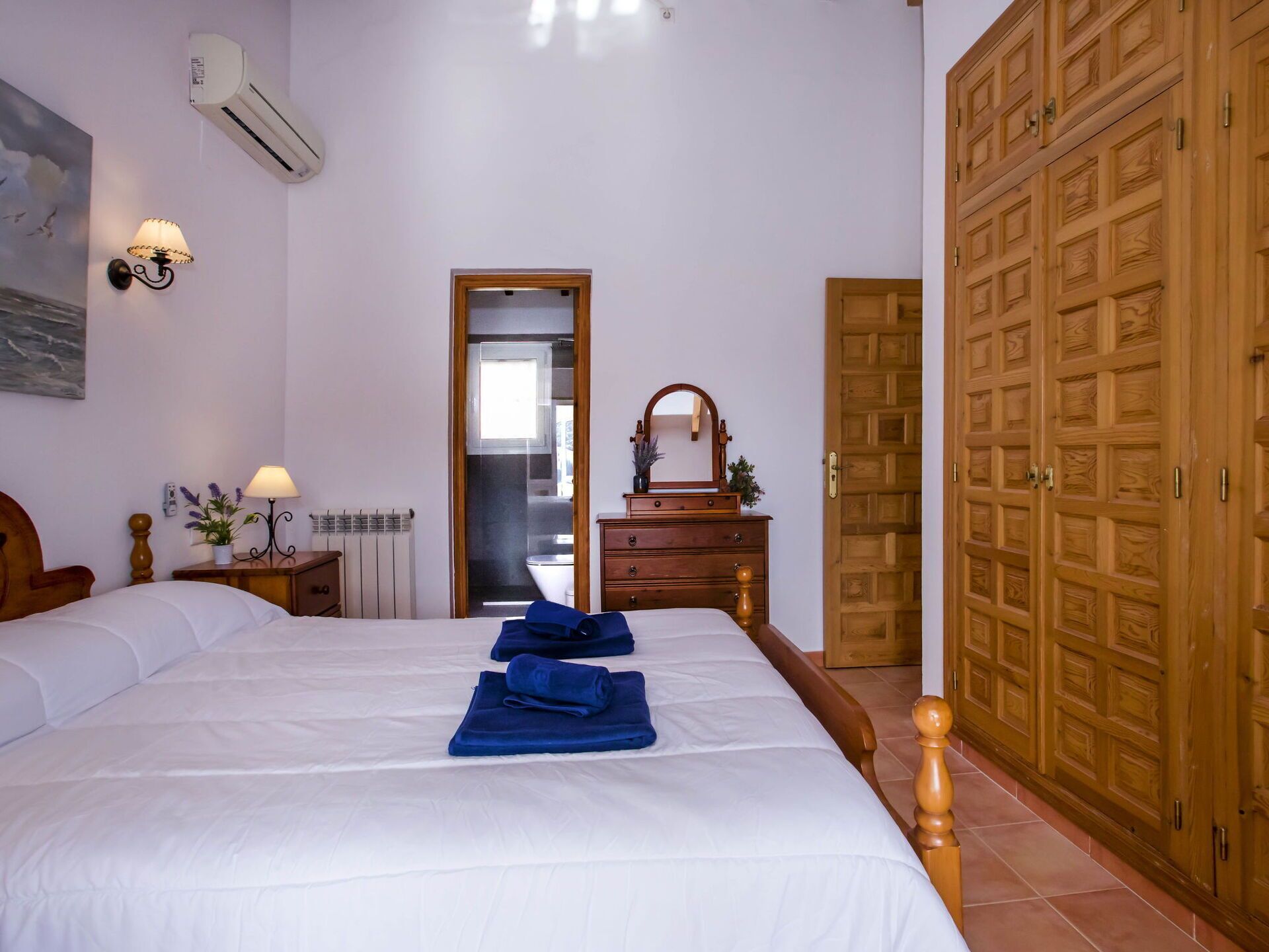Een hotelkamer met een groot bed, een houten garderobe en een badkamer door een open deur zichtbaar.