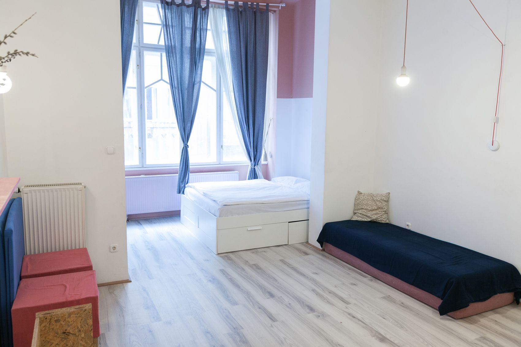 A bedroom with a bed, a small bedside table, a radiator, and a window with curtains.
