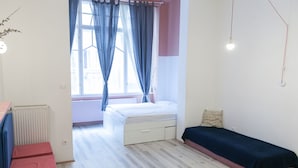 Un dormitori amb llit, taula de nit petita, radiador i finestra amb cortines.