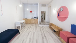 Habitació moderna i ben il·luminada amb terra de fusta, escriptori blanc, llum esfèrica vermella i rellotge de paret rosa.