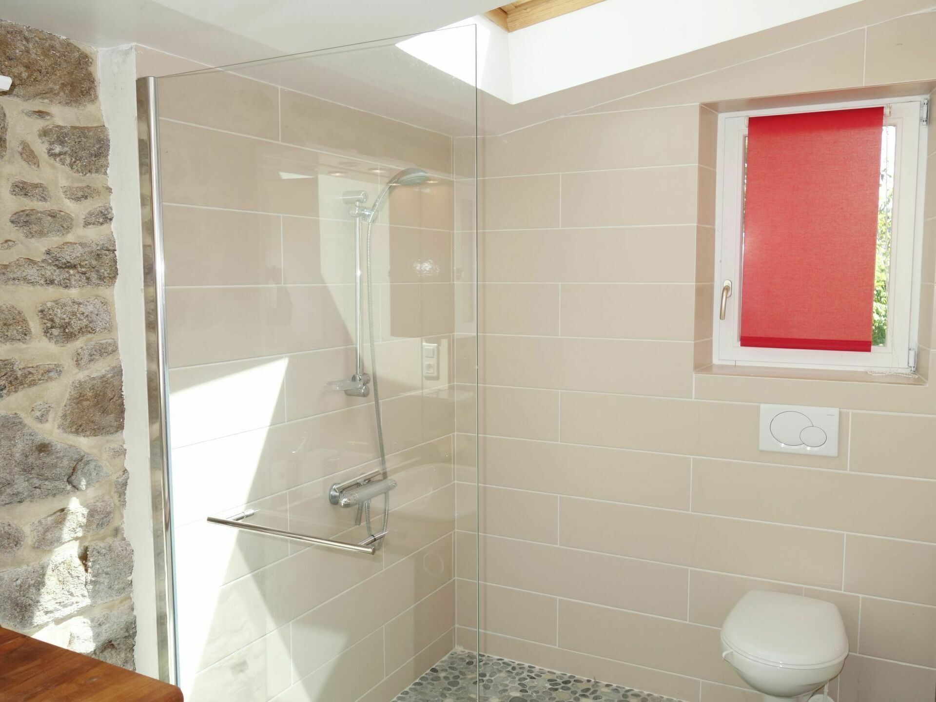 Ein Badezimmer mit Duschkabine aus Glas, einer weißen Toilette und einem Fenster mit rotem Rollo.