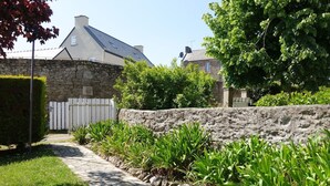 Un chemin de pierres mène à une maison dotée d’un mur en pierre et d’une clôture blanche en bois.