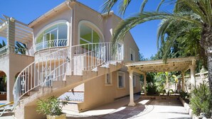 Uma vila em estilo mediterrâneo com um pátio central, um alpendre coberto e uma escadaria que leva ao andar superior.