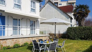 Ein zweistöckiges Haus mit Balkon, einem Esstisch und Stühlen sowie einem Sonnenschirm.
