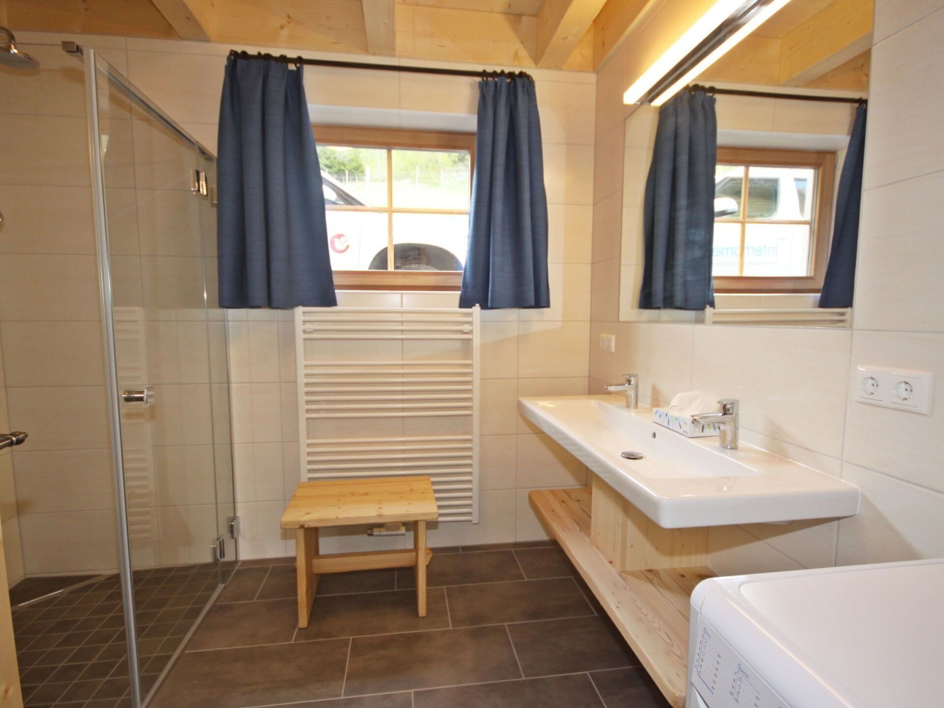 A bathroom with a shower, a sink, a mirror, and a wooden bench.